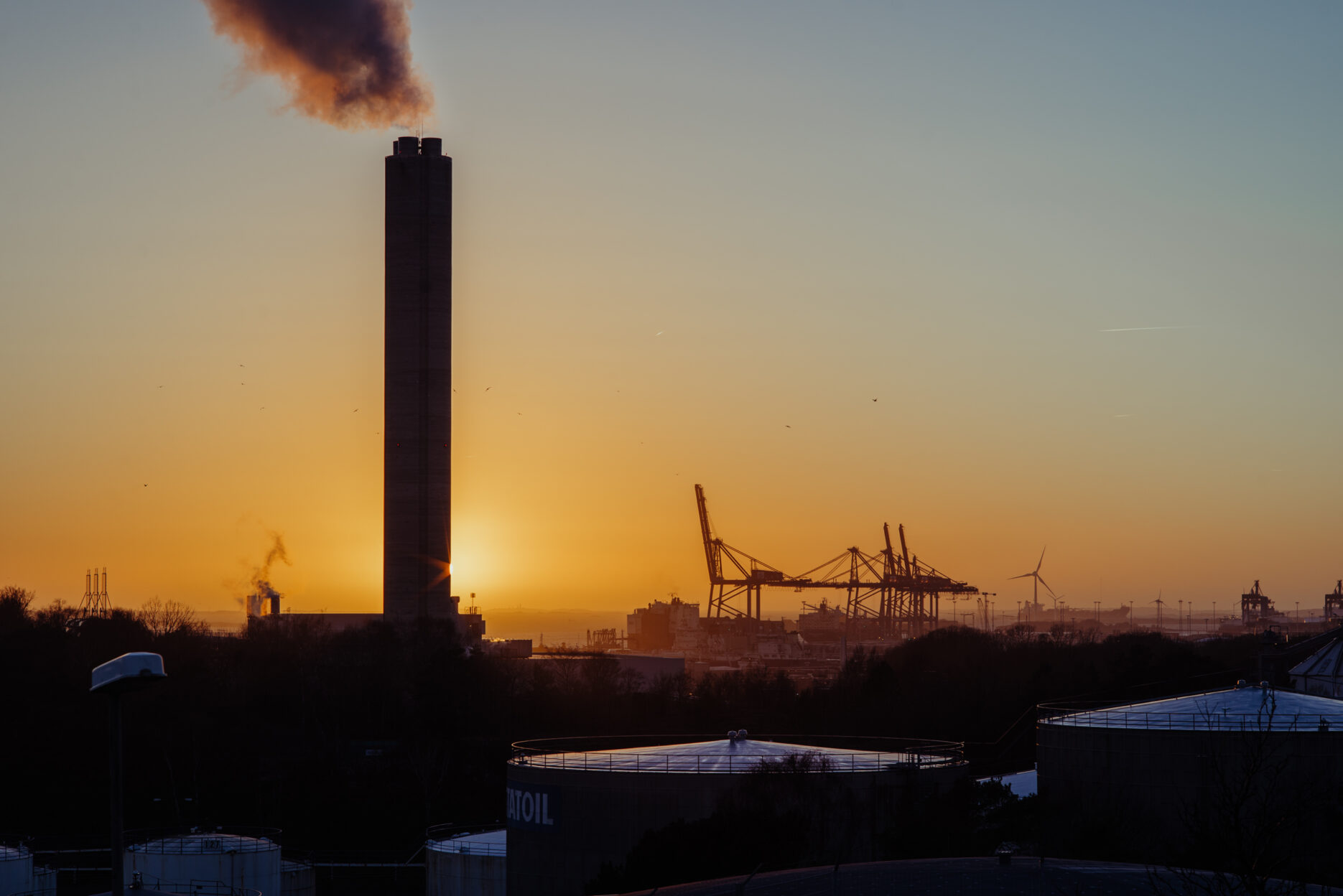 Industrial buildings, cranes and a large chimney against a beautiful sunset