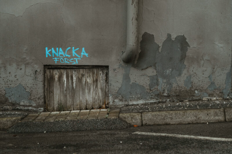 A worn wall with a hatch and the text "Knacka först" (Knock first)