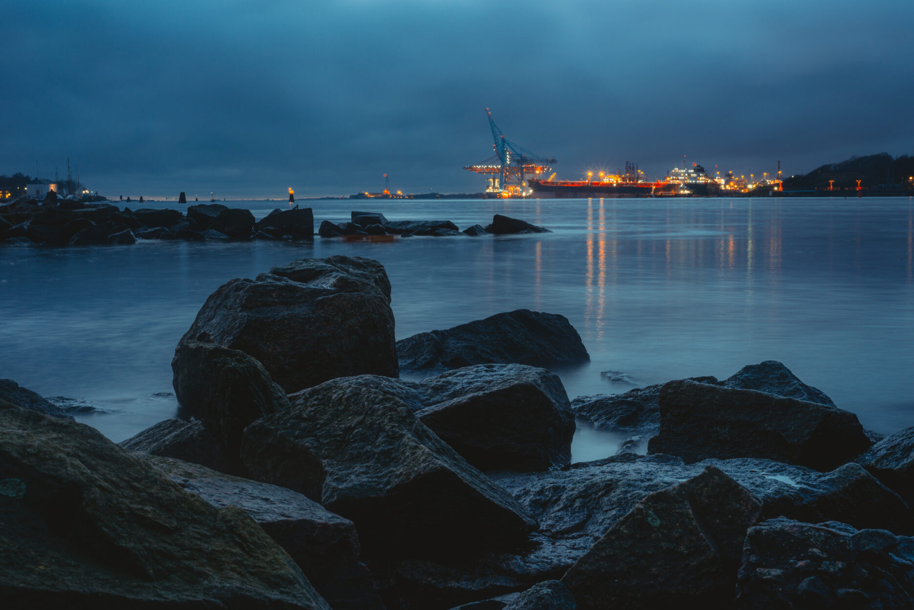 Stones at a coastline. Industrial cranes in the background.