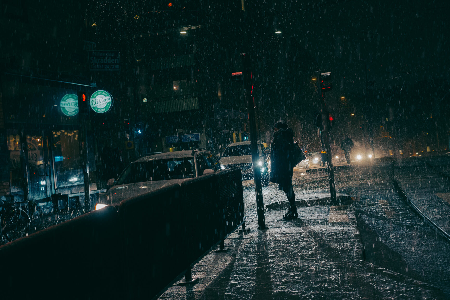 Snow falling over person standing at a pedestrian crossing
