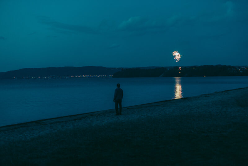 Man standing at a shoreline with fireworks in the background